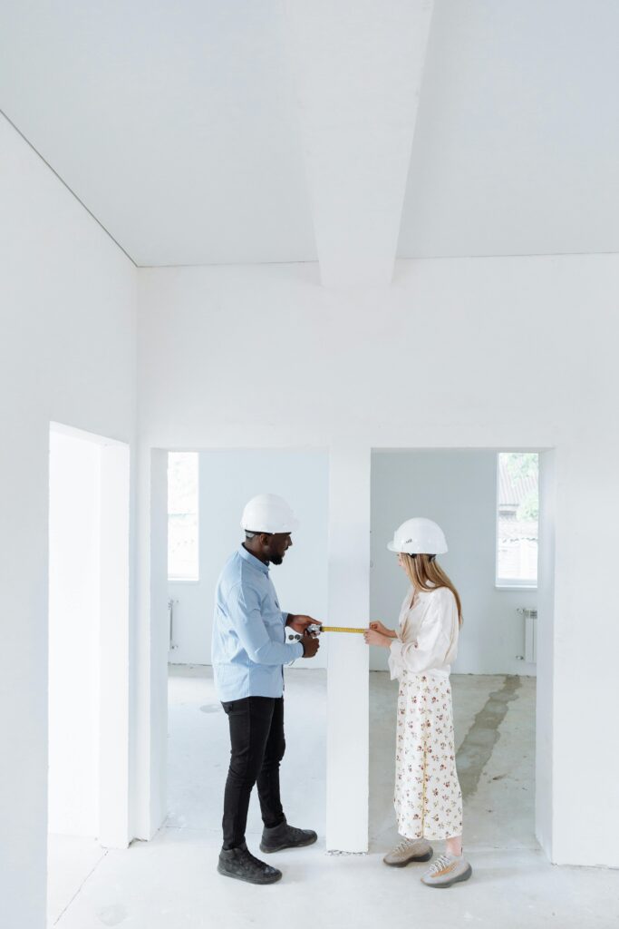 Two professionals in hard hats measuring and discussing a renovation project.